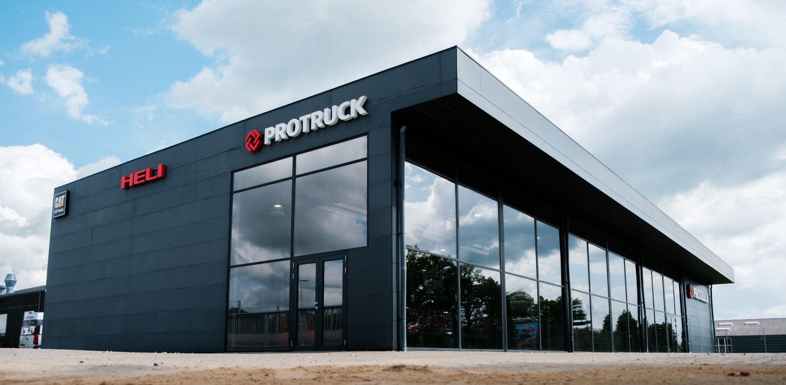 ProTruck showroom med HELI og CAT logo – moderne facade og spejlglas, Skomø-profilering tydelig.