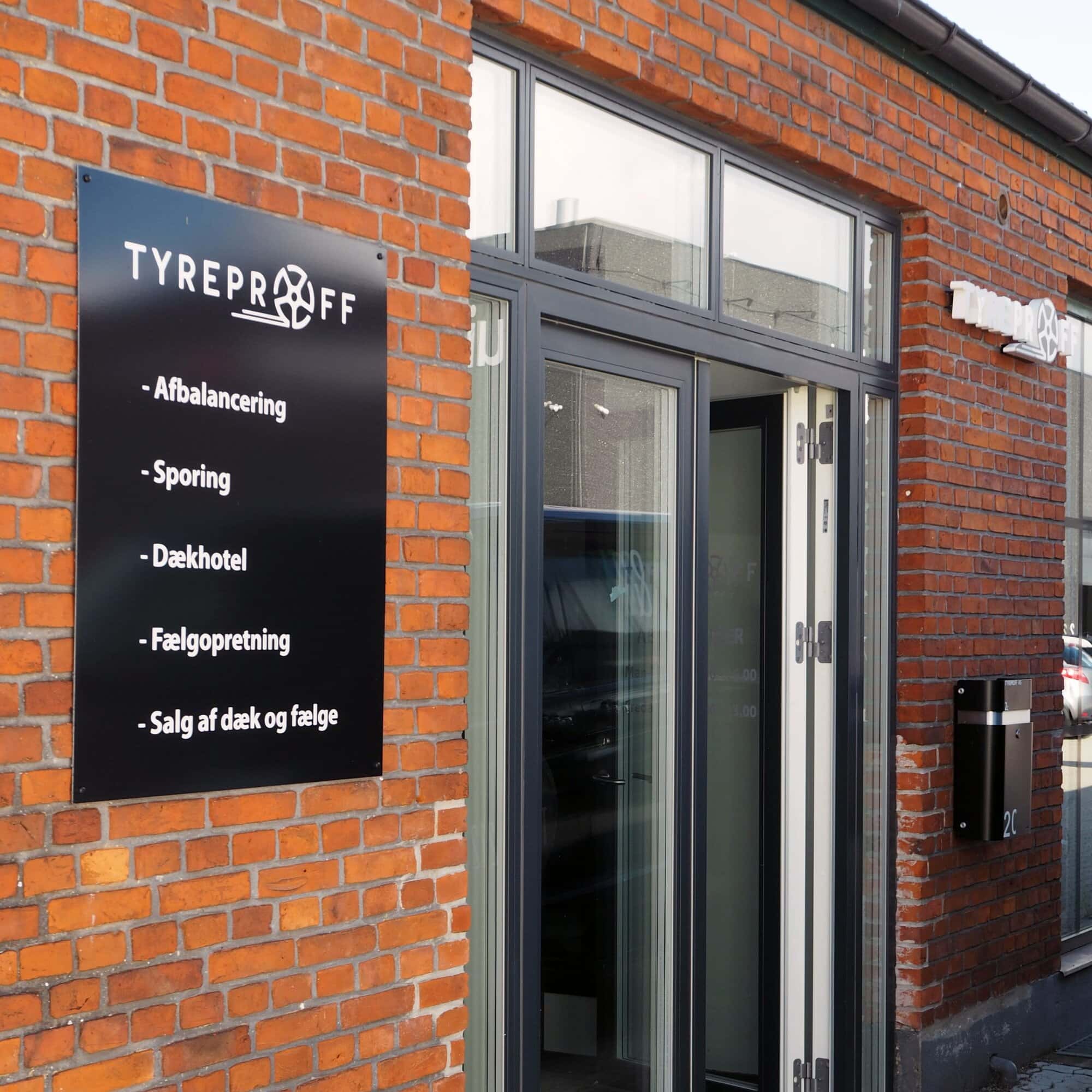 Indgang til Tyreproff med skilt med ydelser på murstensfacade – Skomø